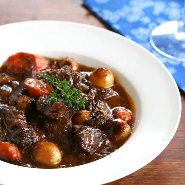 A rich French Boeuf Bourguignon served in a rustic dish, garnished with fresh herbs.