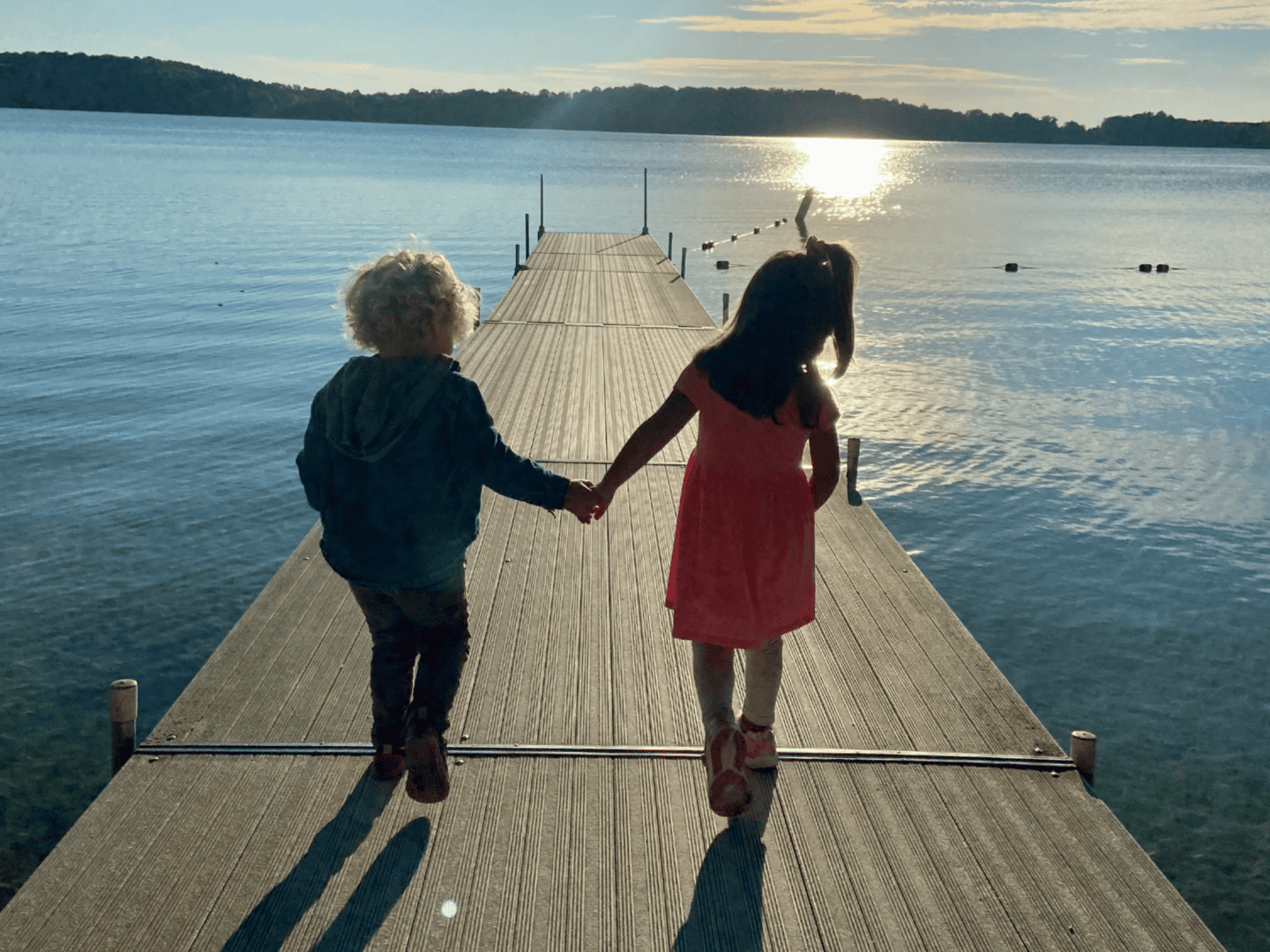 Two children holding hands on a lakeside dock at sunset, enjoying the last days of summer.