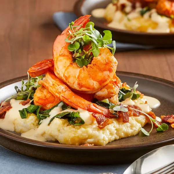 Guests preparing gluten‑free dishes including cauliflower grits with shrimp, chicken piccata, and flourless chocolate cake during a hands‑on cooking class.