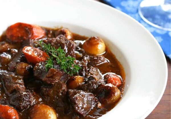 A rich French Boeuf Bourguignon served in a rustic dish, garnished with fresh herbs.