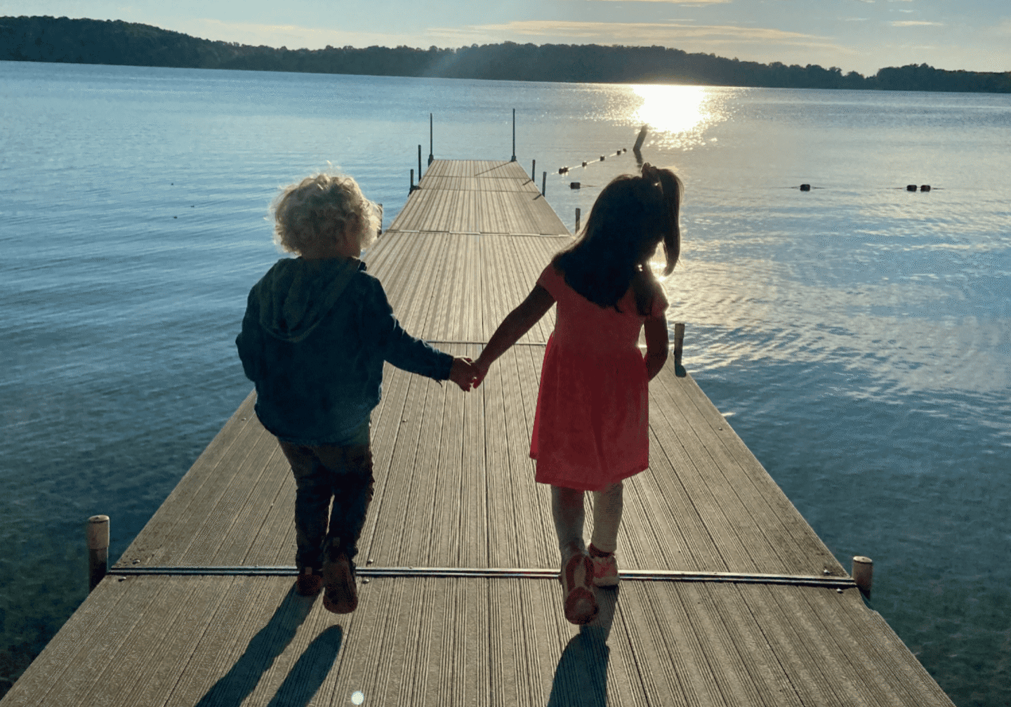 Two children holding hands on a lakeside dock at sunset, enjoying the last days of summer.