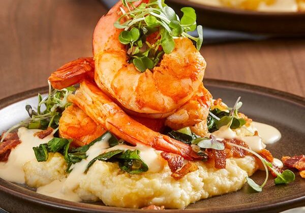 Guests preparing gluten‑free dishes including cauliflower grits with shrimp, chicken piccata, and flourless chocolate cake during a hands‑on cooking class.